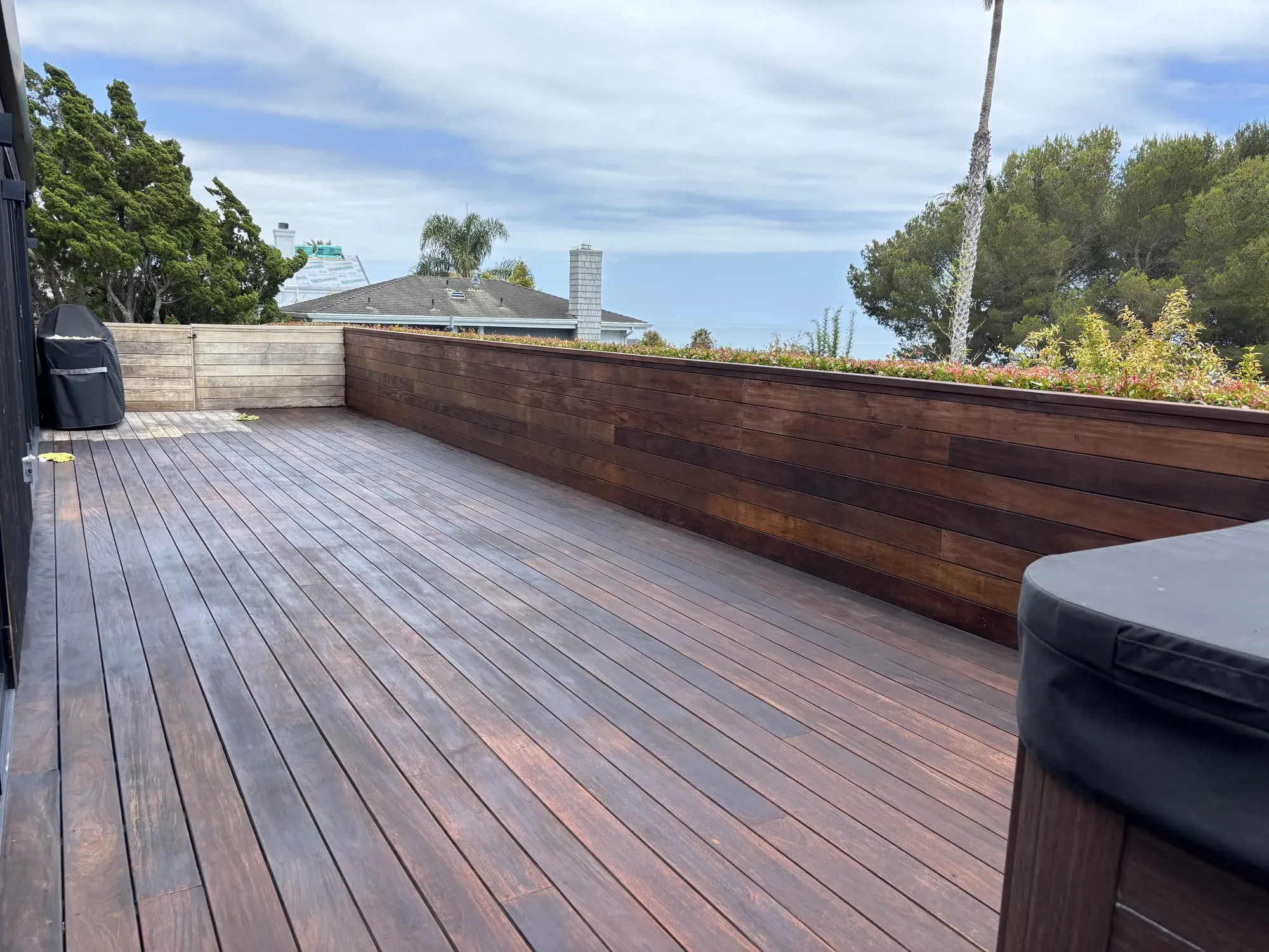 A restored ipe deck oiled to a rich reddish-brown, overlooking greenery and the ocean