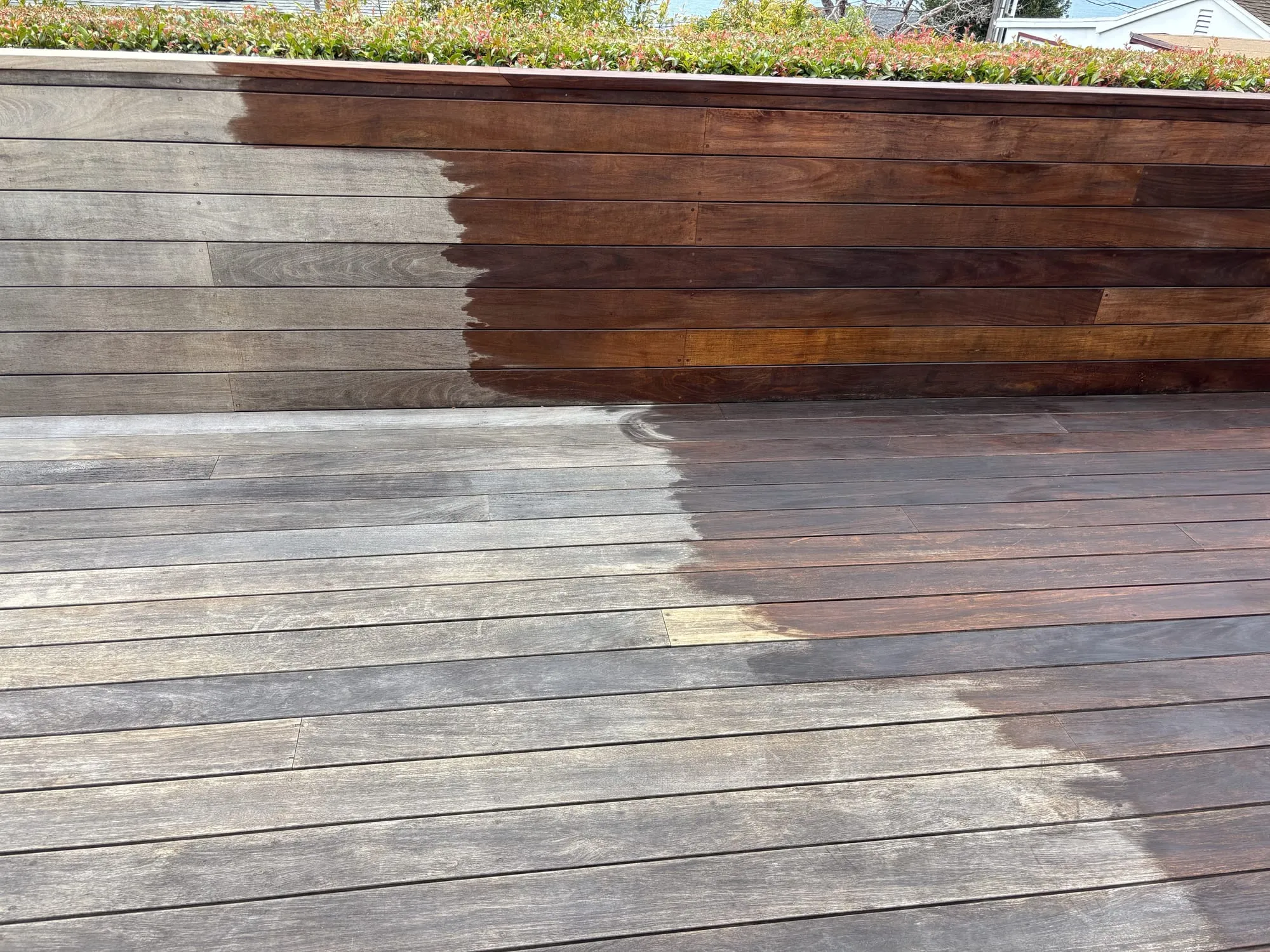 A deck mid-restoration: the left half still gray and weathered, the right half oiled to a rich brown, split down the middle