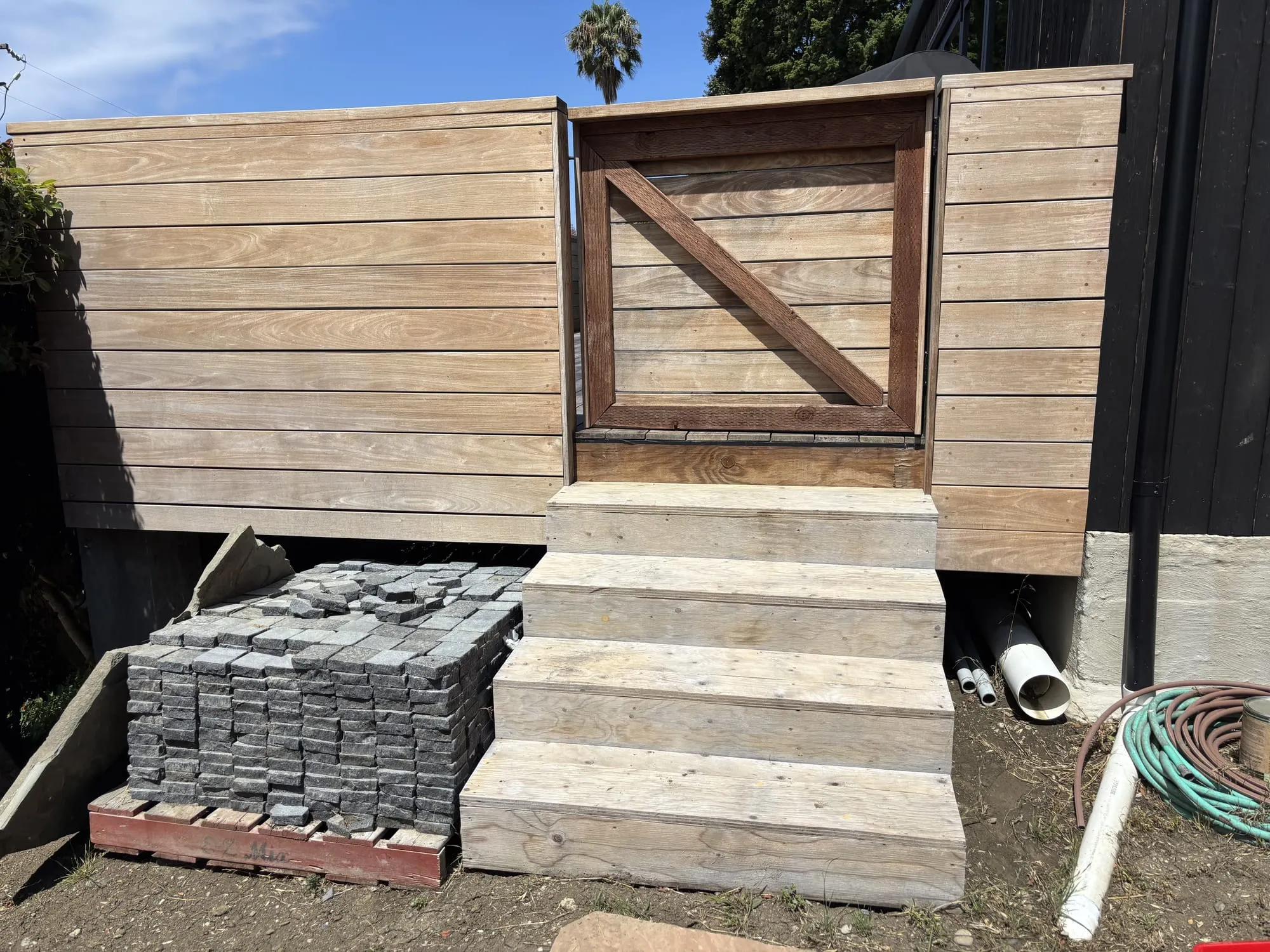 A wood gate and fence before restoration, weathered gray with yard clutter nearby